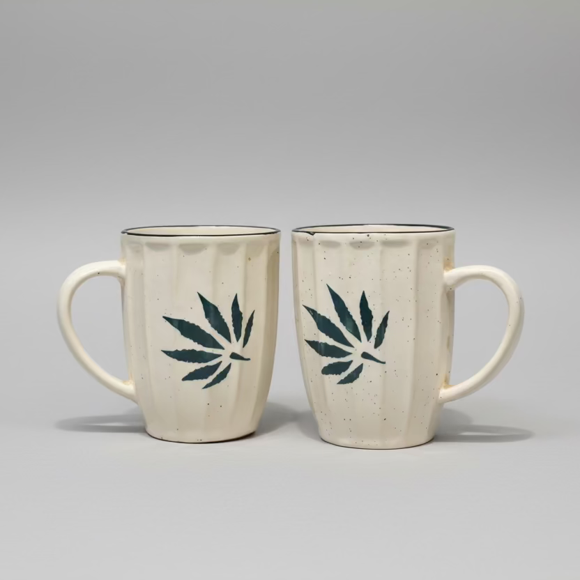 Two ceramic mugs with cannabis leaf designs on a wooden surface.