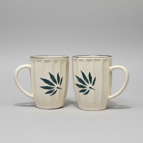 Two ceramic mugs with cannabis leaf designs on a wooden surface.